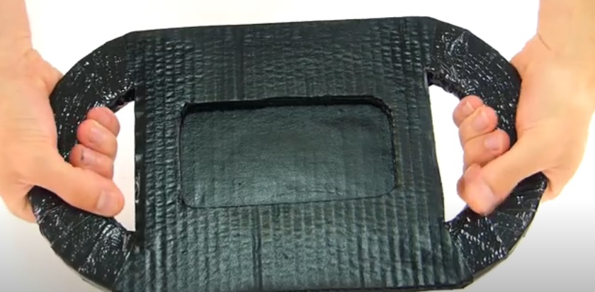 Tutorial: Crea un volante casero para jugar con tu celular 8 Mientras va secando, empezaremos a hacer la base. Recorta una tira de cartón de unos 8 cm de ancho y dóblala en tres partes, dejando una un par de centímetros más larga que las otras dos. Luego refuérzala añadiendo otras capas de cartón, tal cual como hicimos con el volante. Una vez reforzadas, procedemos a pegar el extremo más corto con el más largo con la cinta americana y algo de pegamento. Una vez todo haya secado correctamente, abrimos un agujero en la parte superior de la más larga.